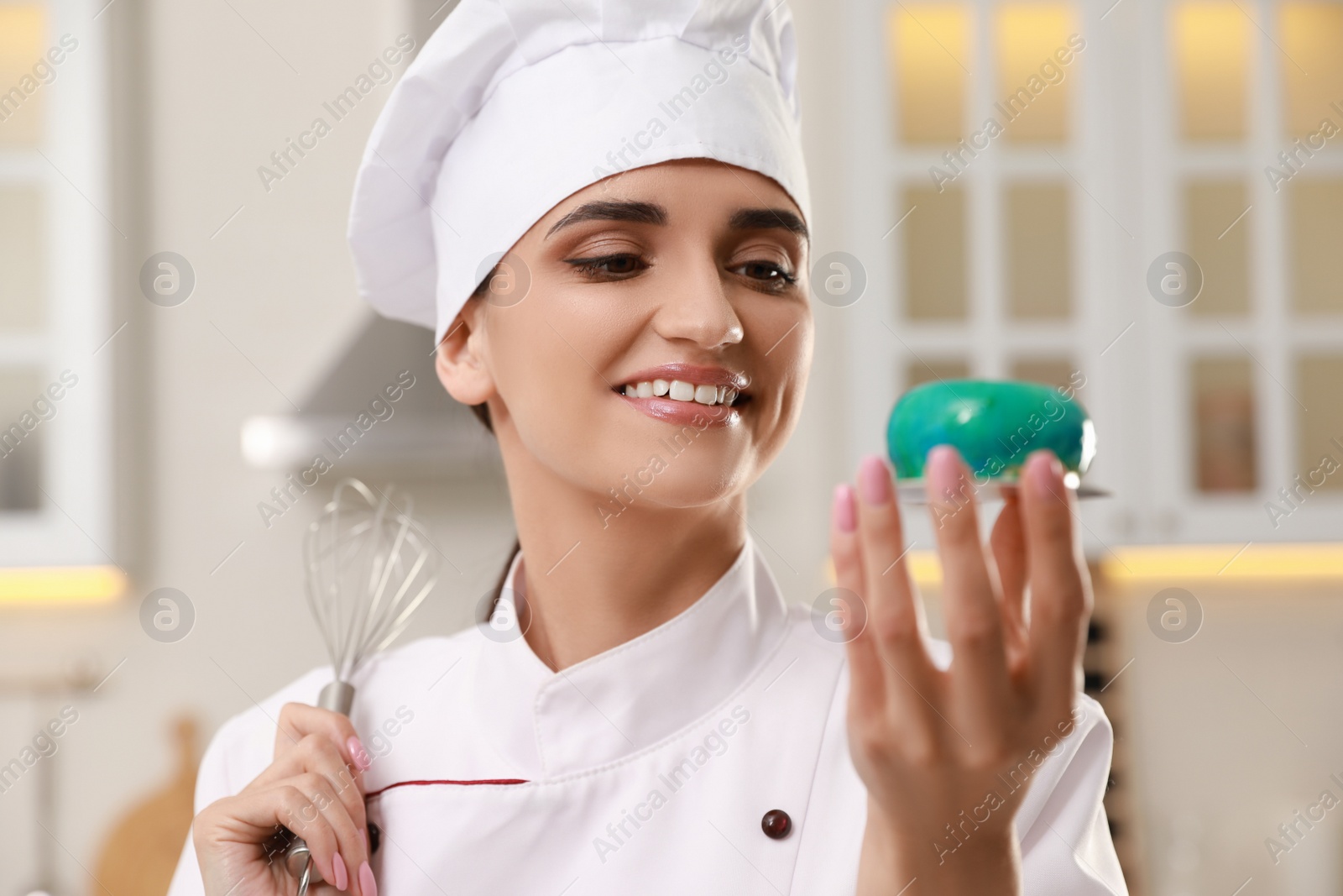 Photo of Happy professional confectioner with delicious cake and whisk in kitchen