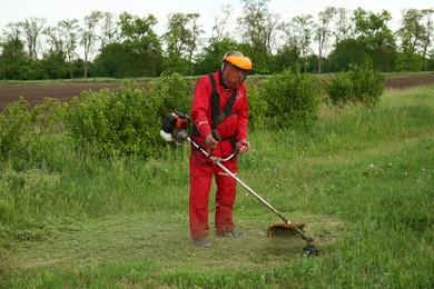 Worker cutting grass with string trimmer outdoors