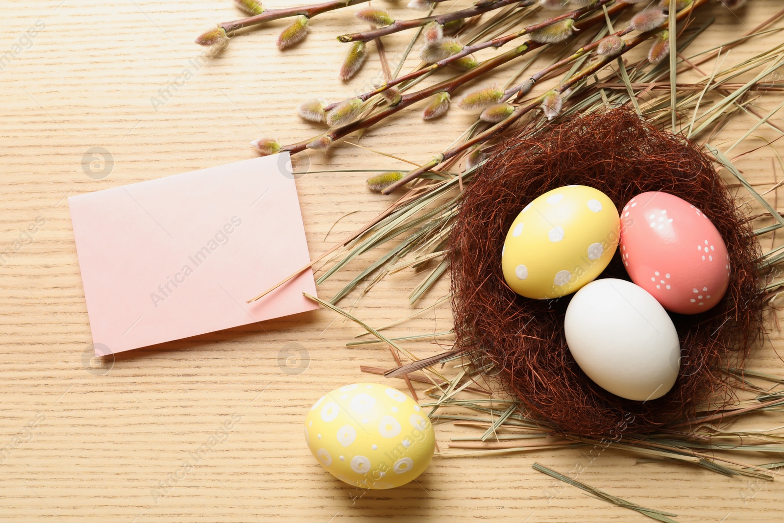 Photo of Flat lay composition with painted Easter eggs and blank card on wooden table, space for text