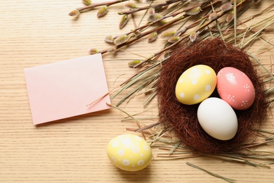 Flat lay composition with painted Easter eggs and blank card on wooden table, space for text