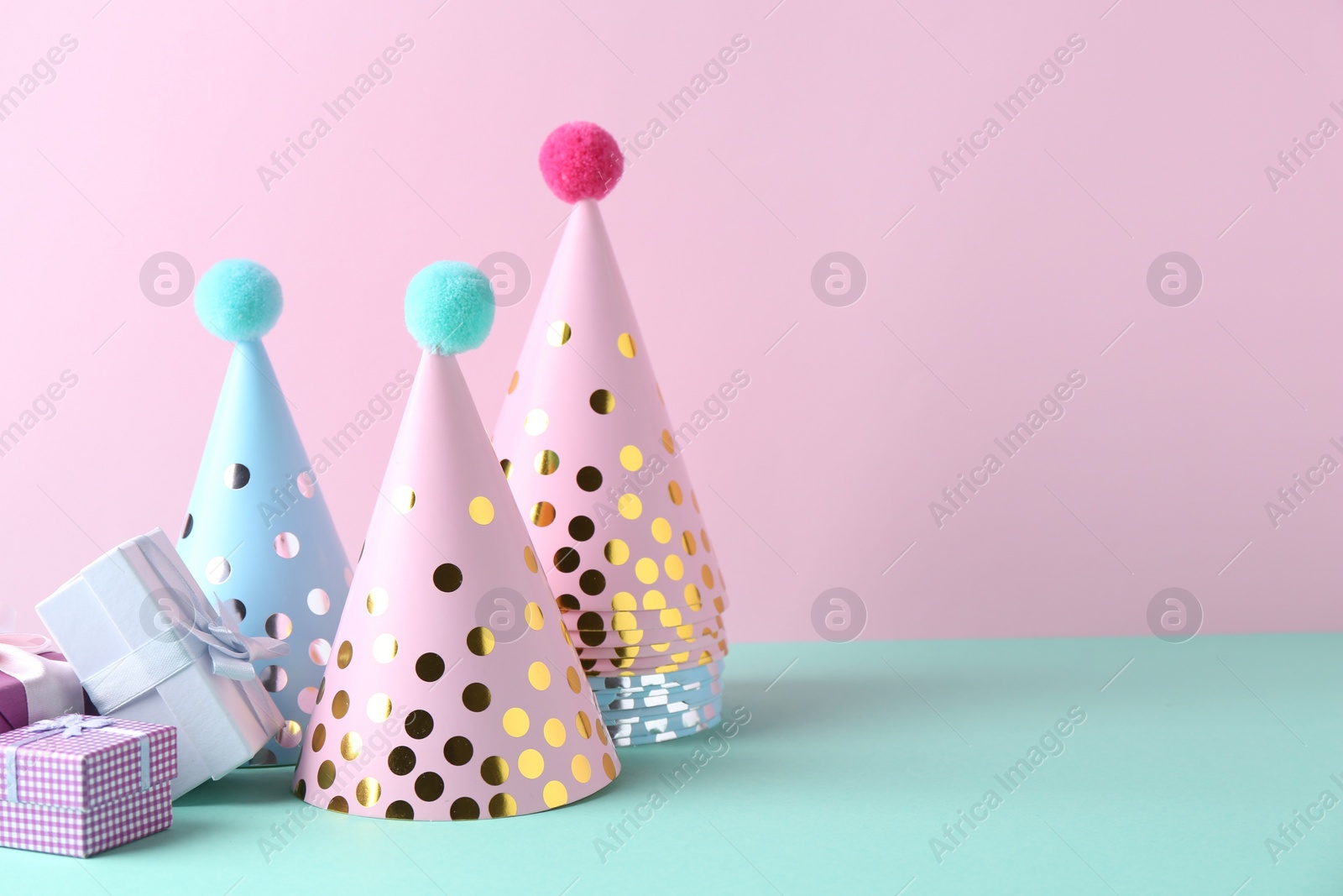 Photo of Party hats and gift boxes on color background, space for text