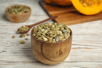 Photo of Bowl of raw pumpkin seeds on white wooden table