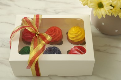 Box with delicious colorful cupcakes and beautiful flowers on white marble table