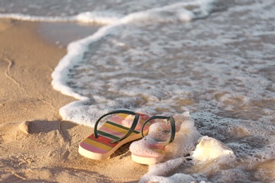 Photo of Stylish flip flops and shell on sand near sea, space for text. Beach accessories