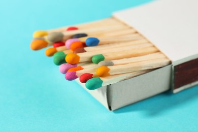 Photo of Matches with colorful heads in box on light blue background, closeup