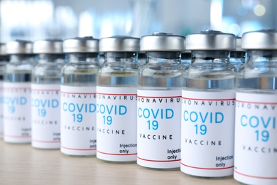 Photo of Glass vials with COVID-19 vaccine on wooden table