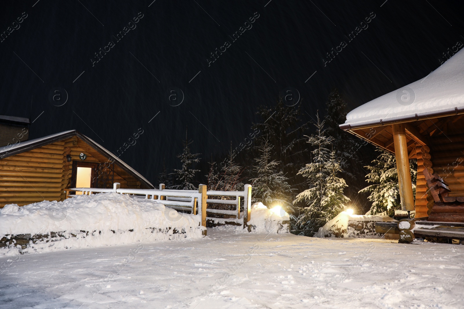 Photo of Wooden cottage and bridge covered with snow near fir forest at night. Winter vacation