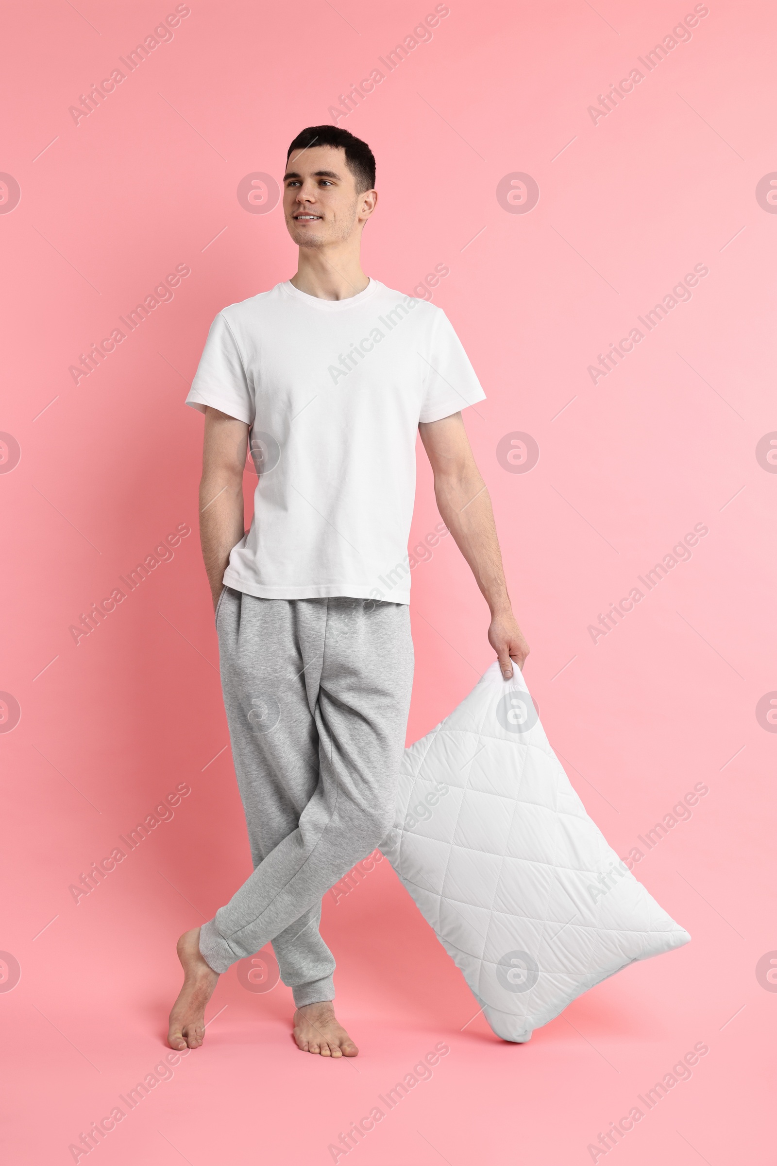 Photo of Happy man in pyjama holding pillow on pink background