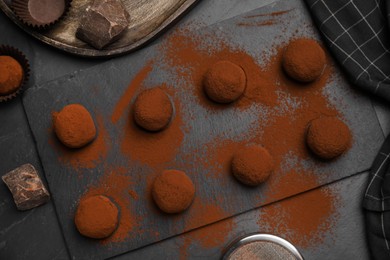 Delicious chocolate truffles powdered with cocoa on black table, flat lay