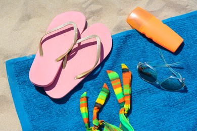 Soft blue beach towel with flip flops, bottle of sunscreen and sunglasses, flat lay