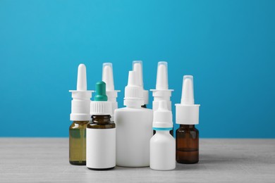 Photo of Nasal sprays in different bottles on white wooden table against light blue background