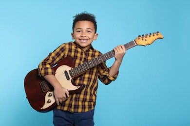 Cute African-American boy with electric guitar on turquoise background