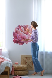 Young interior designer painting flower on wall in modern room