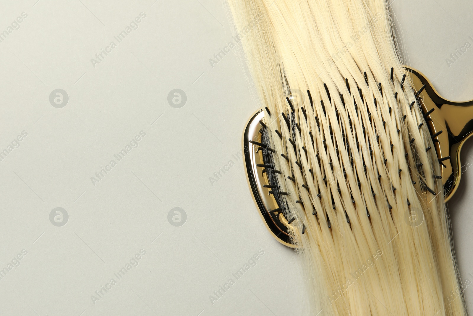 Photo of Stylish brush with blonde hair strand on light grey background, top view. Space for text