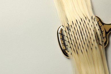 Stylish brush with blonde hair strand on light grey background, top view. Space for text