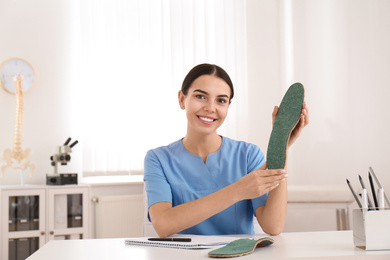 Photo of Young female orthopedist showing insole in clinic