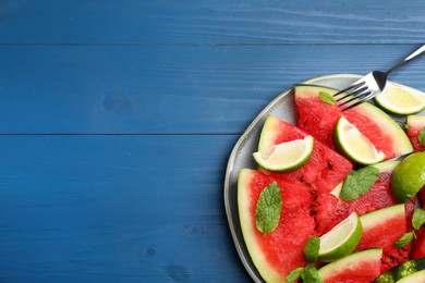 Photo of Plate with juicy watermelon and lime on blue wooden table, top view. Space for text