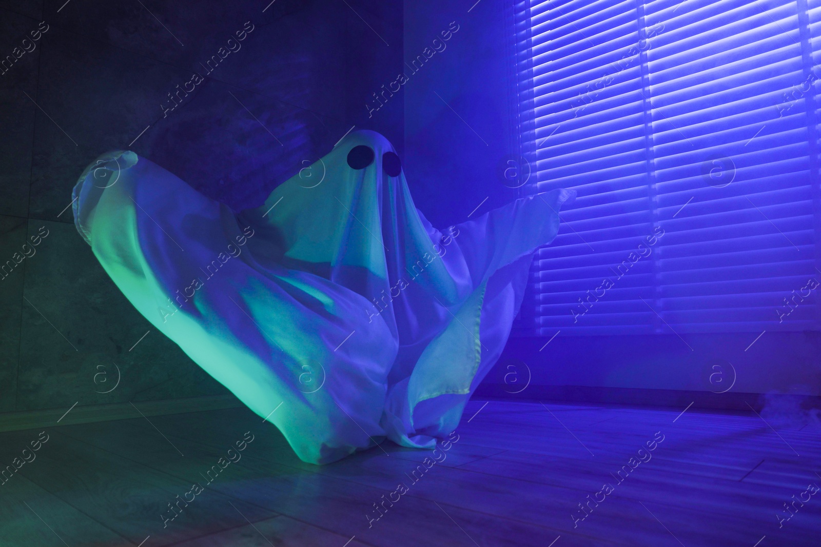 Photo of Creepy ghost. Woman covered with sheet near window in blue light