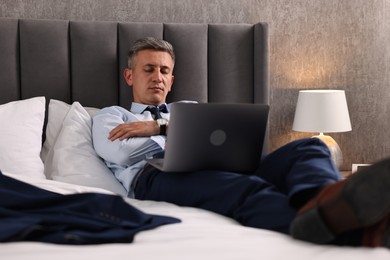 Businessman with laptop sleeping on bed indoors