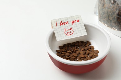 Photo of Feeding bowl with dry cat food and cute note I Love You on white background. Space for text