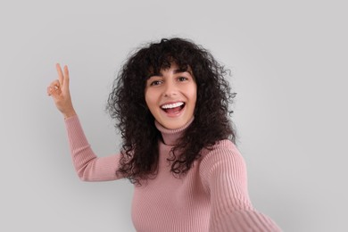 Beautiful young woman taking selfie on light grey background