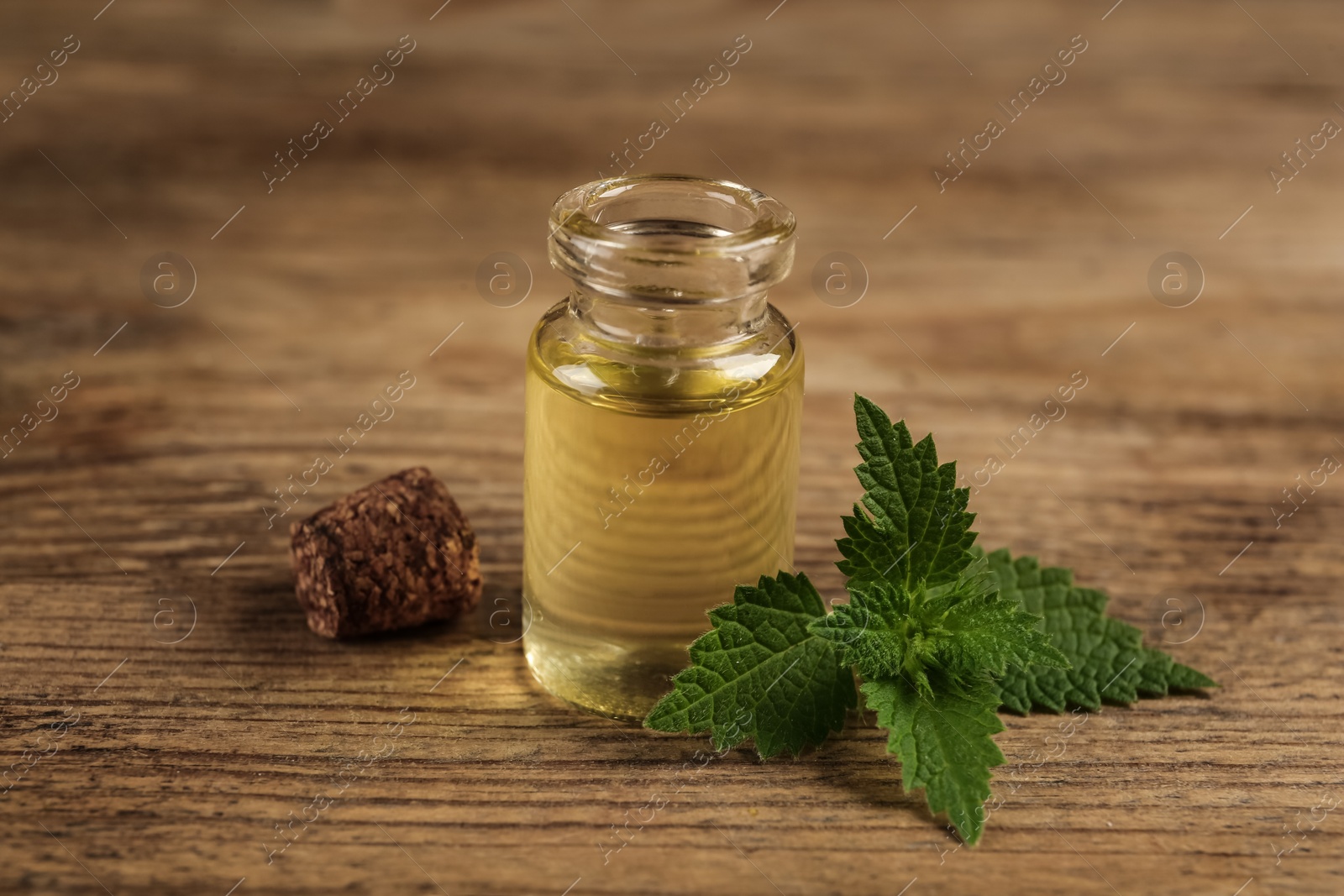 Photo of Glass bottle of nettle oil with leaves on wooden table, closeup