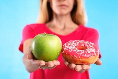 Photo of Woman choosing between doughnut and fresh apple on light blue background, closeup