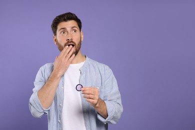Emotional man holding condom on purple background, space for text. Safe sex