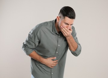 Man suffering from stomach ache and nausea on beige background. Food poisoning