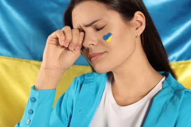 Photo of Sad young woman with face paint near Ukrainian flag, closeup