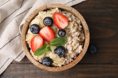 Photo of Tasty oatmeal with strawberries, blueberries and almond petals in bowl on wooden table, top view