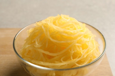 Bowl with cooked spaghetti squash on wooden board