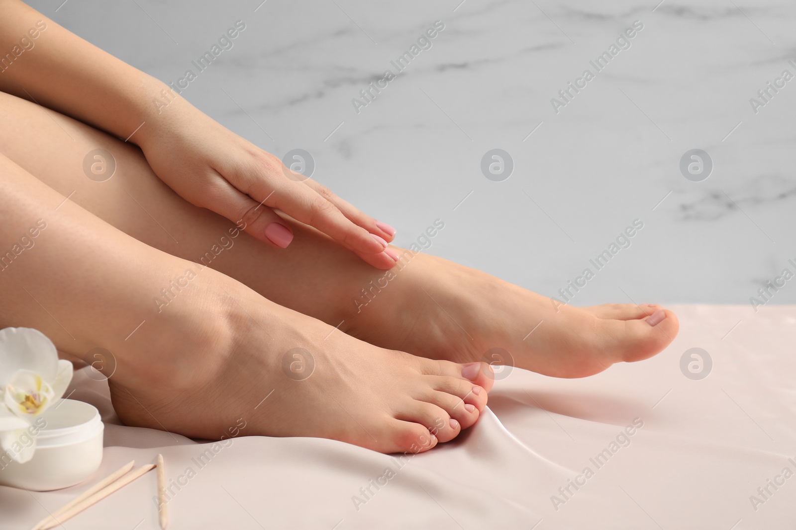 Photo of Woman with neat toenails after pedicure procedure on silk fabric, closeup