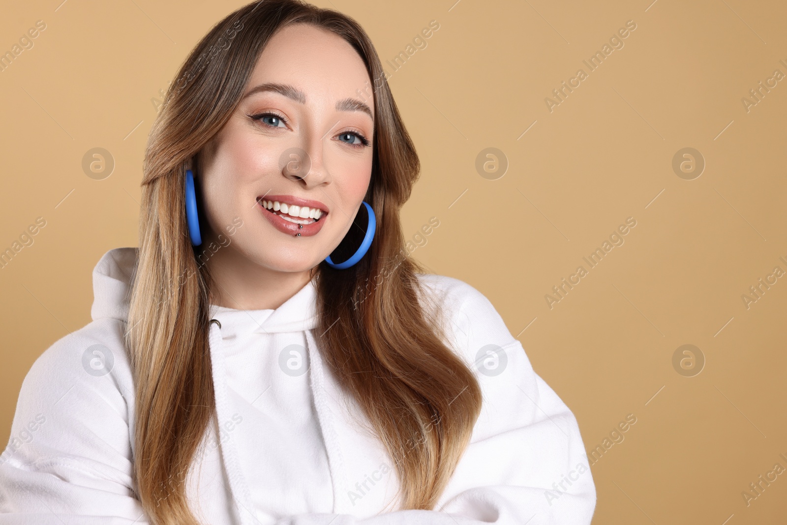Photo of Young woman with lip piercing on beige background. Space for text