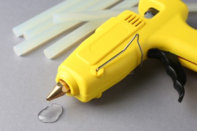 Photo of Melted glue dripping out of hot gun nozzle near sticks on grey background, closeup