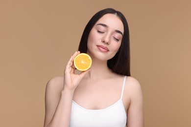 Beautiful young woman with piece of orange on beige background