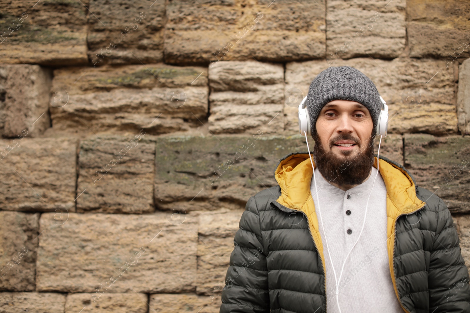 Photo of Mature man with headphones listening to music near stone wall. Space for text