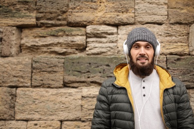 Mature man with headphones listening to music near stone wall. Space for text