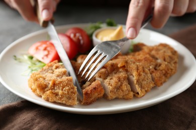 Photo of Woman eating delicious schnitzel at table, closeup