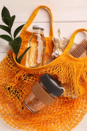 Net bag with different items on white wooden table, top view. Conscious consumption