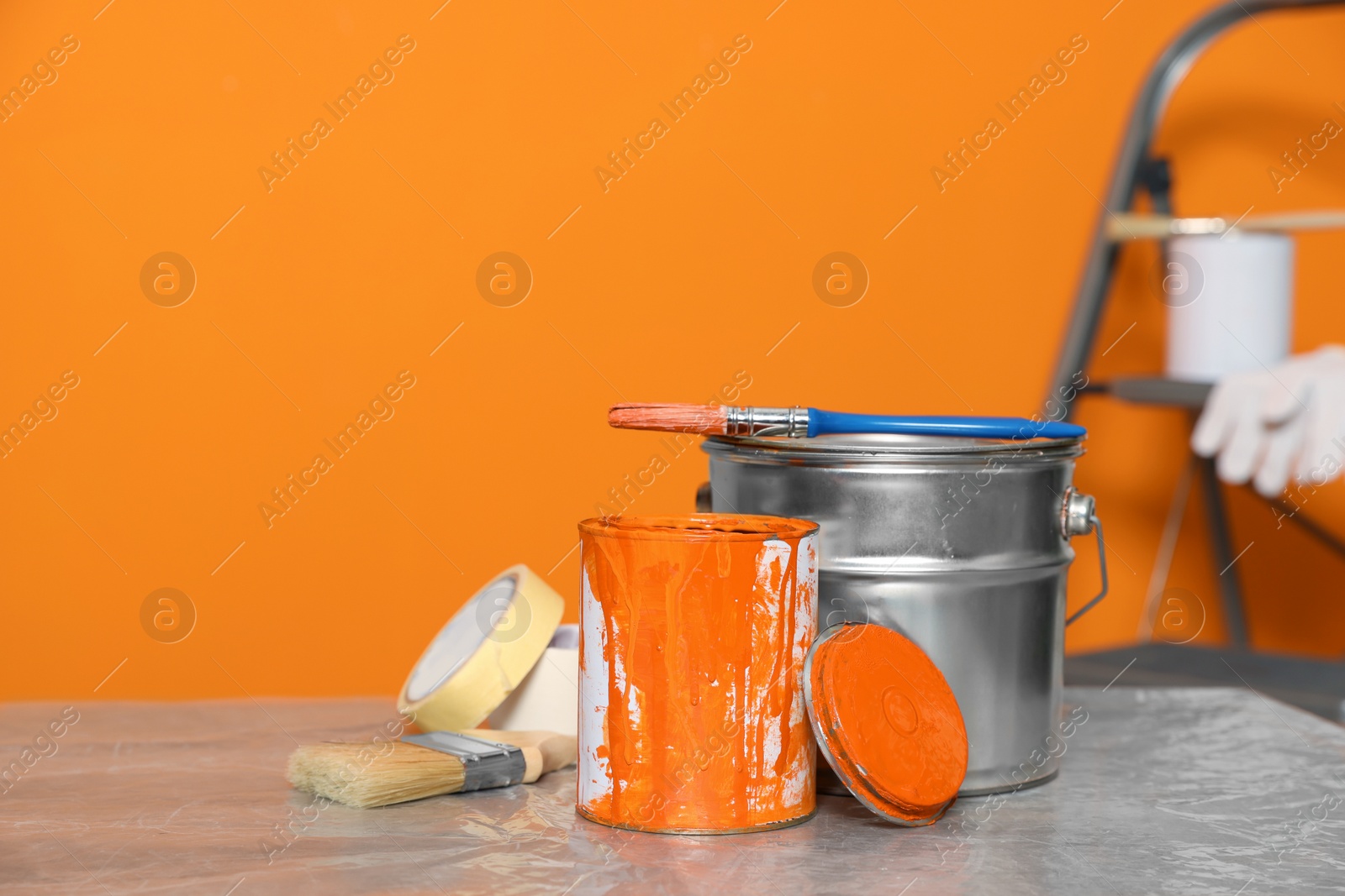 Photo of Can with paint, brush and renovation equipment on table against orange background. Space for text