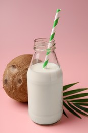 Photo of Glass bottle of delicious vegan milk, coconut and leaf on pink background