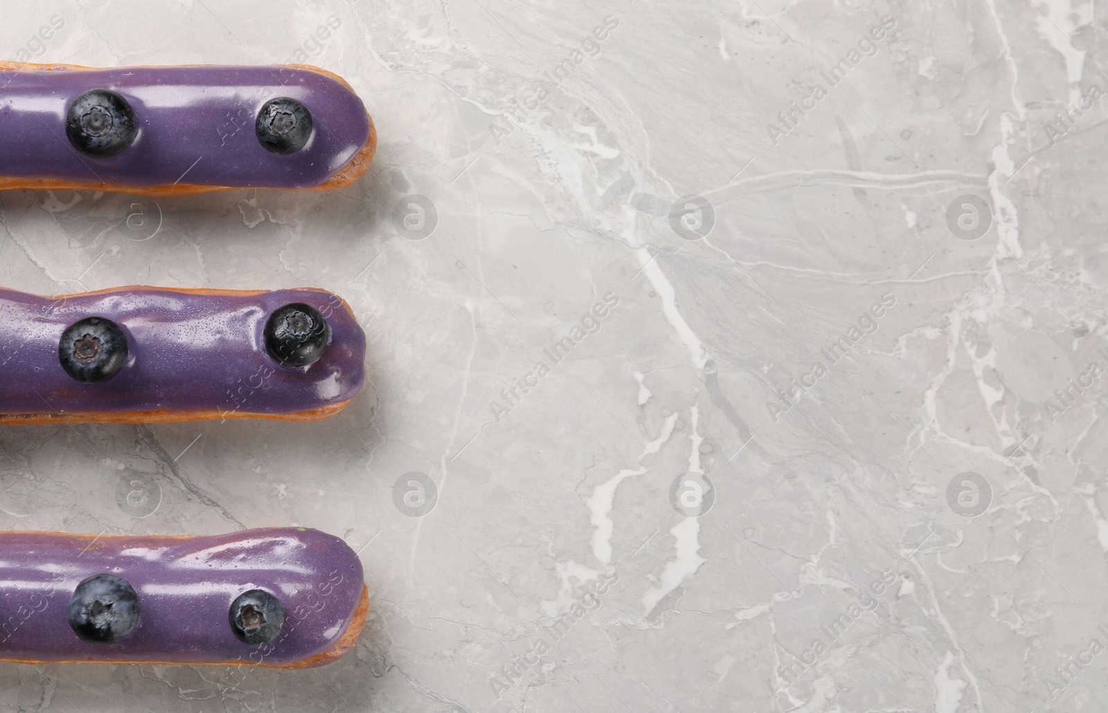 Photo of Tasty glazed eclairs with blueberries on grey marble table, flat lay. Space for text