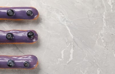 Photo of Tasty glazed eclairs with blueberries on grey marble table, flat lay. Space for text