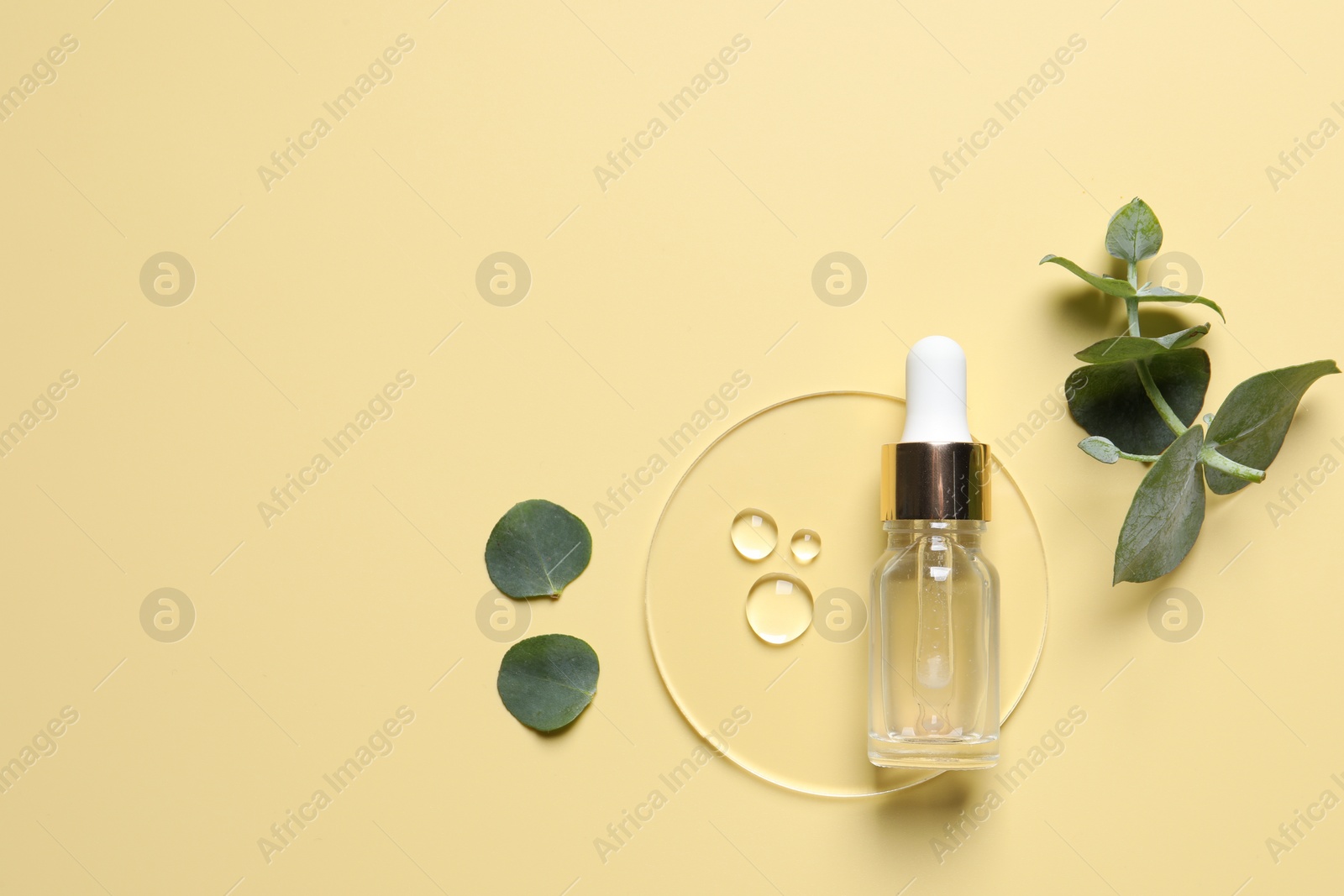 Photo of Bottle of cosmetic serum and green leaves on pale yellow background, flat lay. Space for text