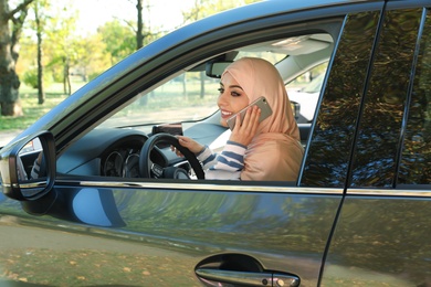 Photo of Muslim woman talking on phone in driver's seat of car