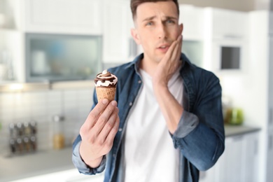 Photo of Young man with sensitive teeth and cold ice cream in kitchen