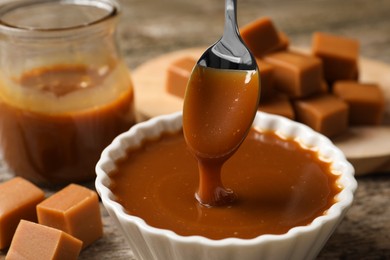 Photo of Taking tasty salted caramel with spoon from bowl at table, closeup