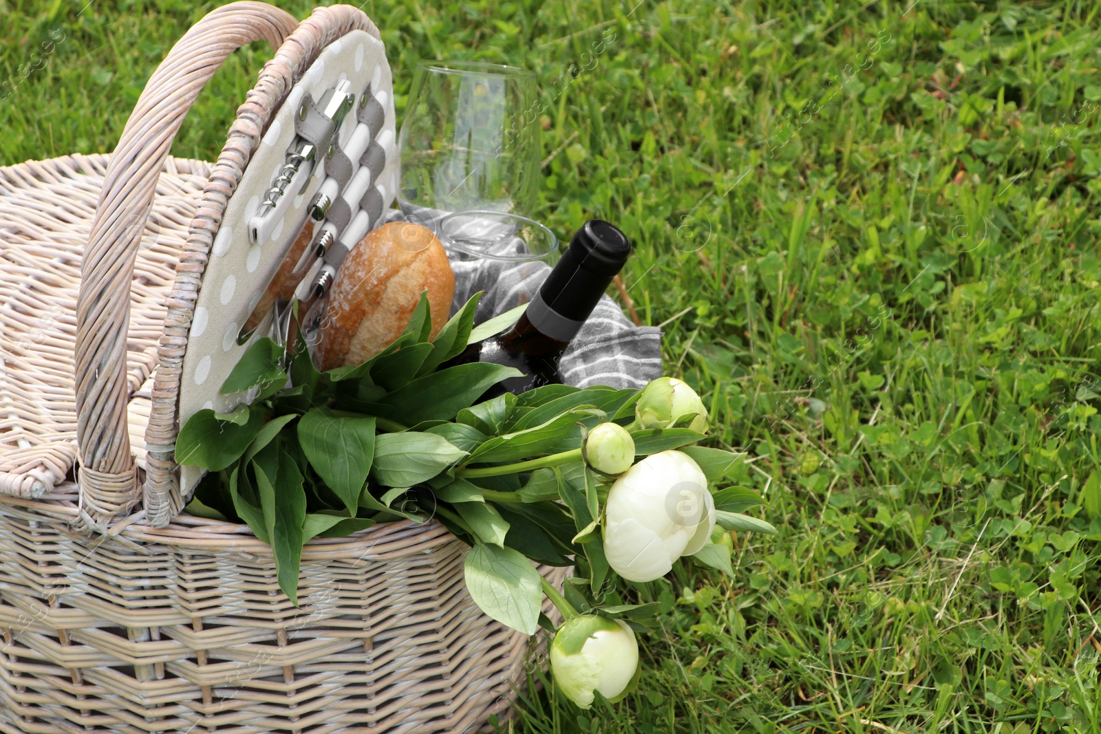 Photo of Picnic basket with wine, bread and flowers on green grass outdoors