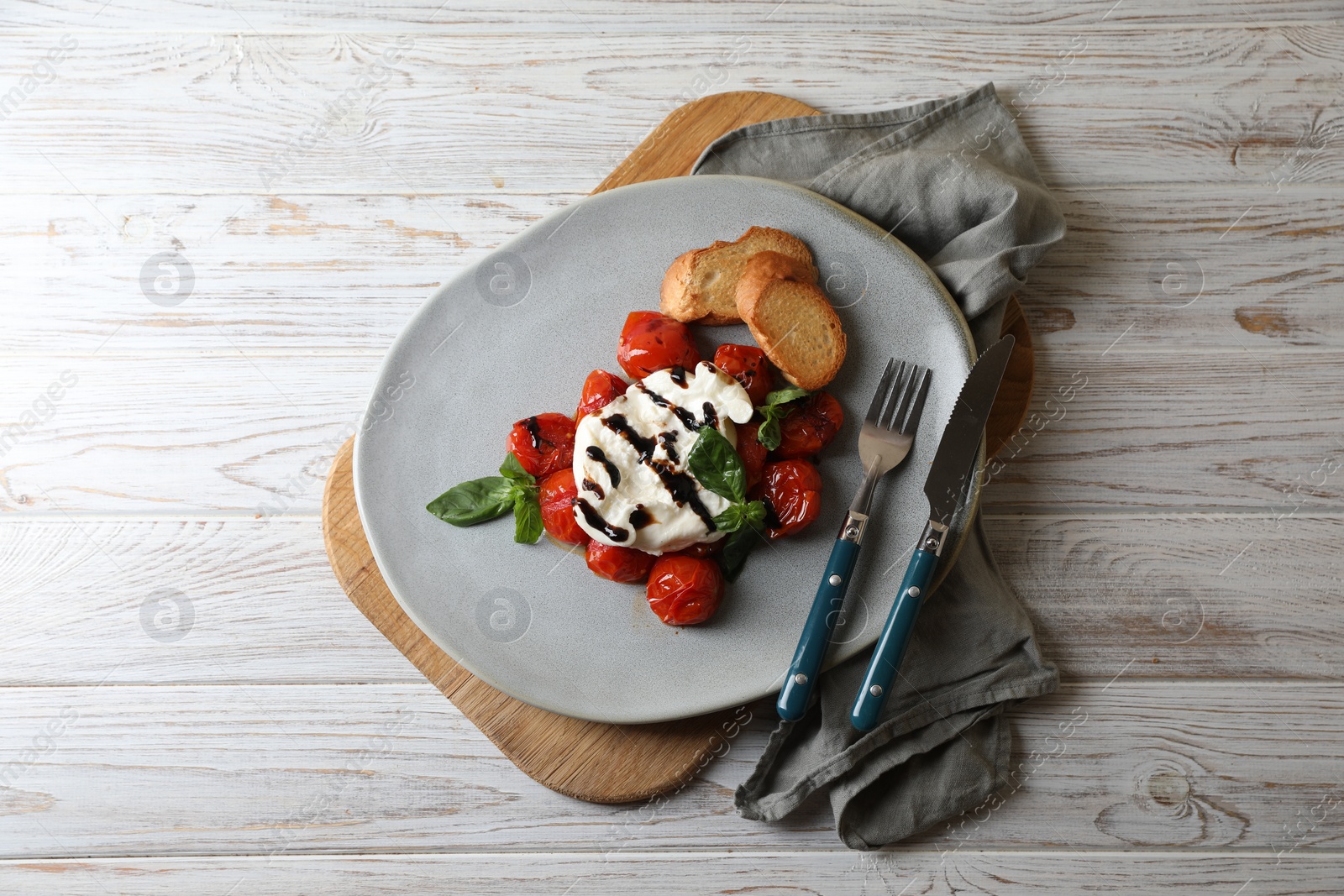 Photo of Delicious burrata cheese served with tomatoes, croutons and basil sauce on white wooden table, top view